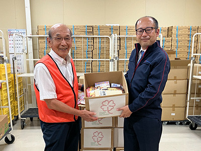 セカンドハーベスト名古屋 前川理事長(左)に食品などを手渡す 当社総務部長の佐藤 真臣