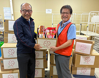 セカンドハーベスト名古屋 松岡理事長（右）に食品などを手渡す 当社 総務部長の佐藤 真臣