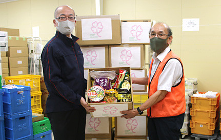 セカンドハーベスト名古屋 前川理事長(右)に食品などを手渡す当社総務部長の羽賀